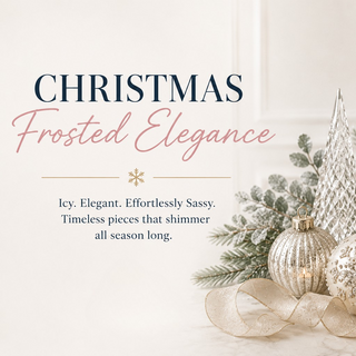 A styled holiday tabletop arrangement with frosted silver and white Christmas ornaments, small frosted trees, a white poinsettia, greenery, and lit glass candle holders on a light neutral background. Text on the left reads “CHRISTMAS Frosted Elegance.
