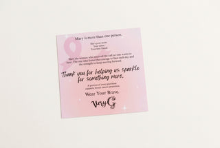 A pink awareness ribbon card with a memorial poem and the text 'Wear Your Brave' by Very G, placed on a light gray surface.